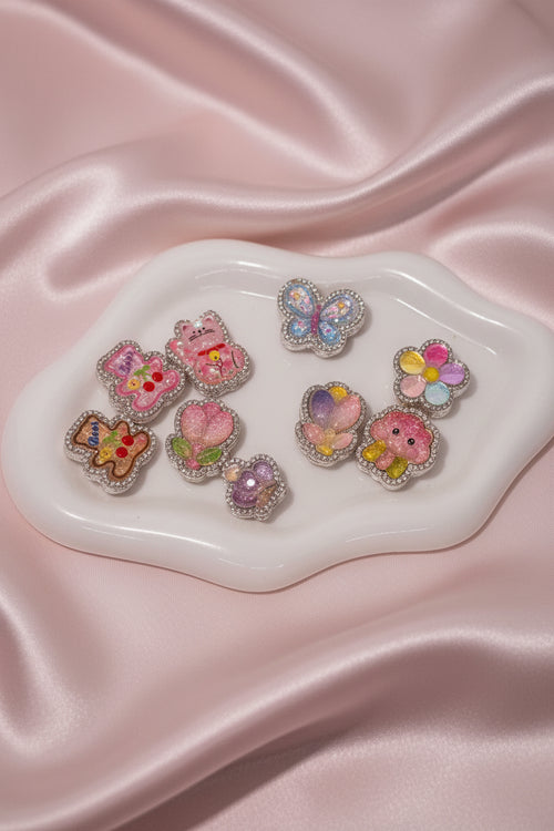 Cute handmade beaded charms with glitter, flowers, cats, and butterflies on pink satin for DIY accessories.