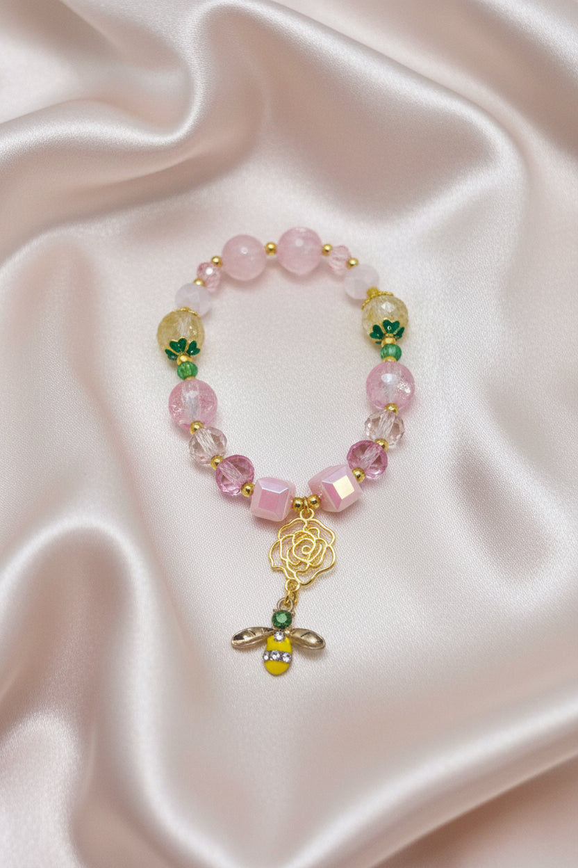 Handmade beaded bracelet with pink beads, gold bee charm, and rose pendant on satin background