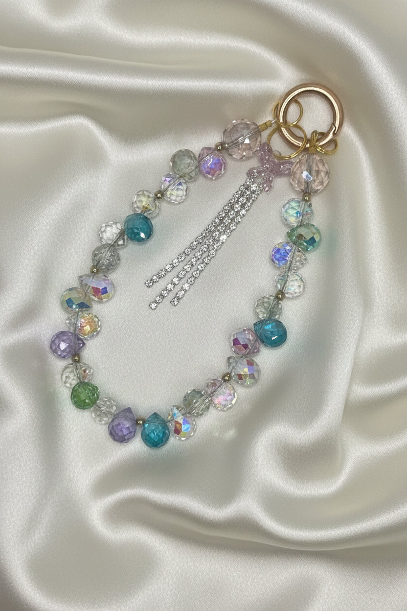 Handmade beaded keychain with iridescent crystals, pastel beads, and tassel on satin background