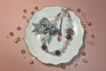 Handmade beaded necklace with gray bow, crystal charms, and assorted beads on white plate