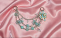 Handmade beaded necklace with blue floral charms and pearl accents on pink satin, perfect for DIY accessories.