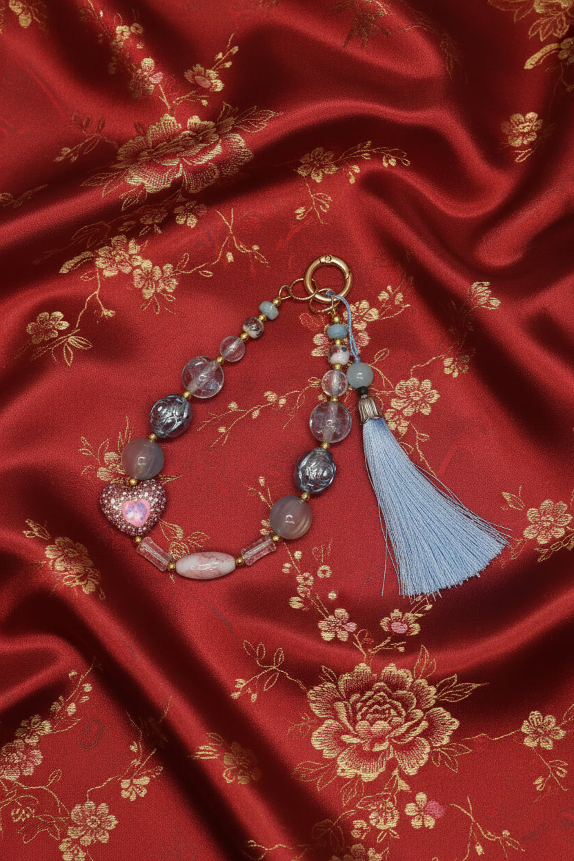 Handmade beaded keychain with heart charm and blue tassel on red floral fabric