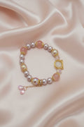 Handmade beaded bracelet with pink pearls, gold accents, and cat charm on satin background