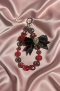 Handmade beaded keychain with red and black beads, bow, and crystal charm on pink satin