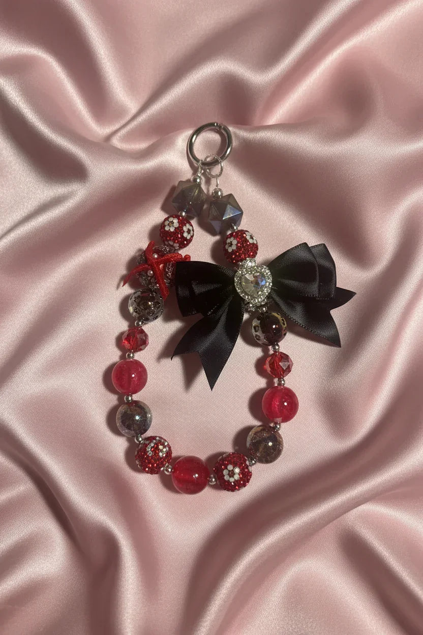 Handmade beaded keychain with red and black beads, bow, and crystal charm on pink satin