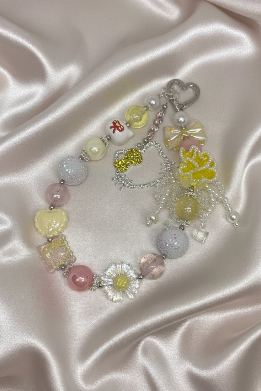 Handmade beaded keychain with pastel charms, glitter beads, and floral accents on satin background