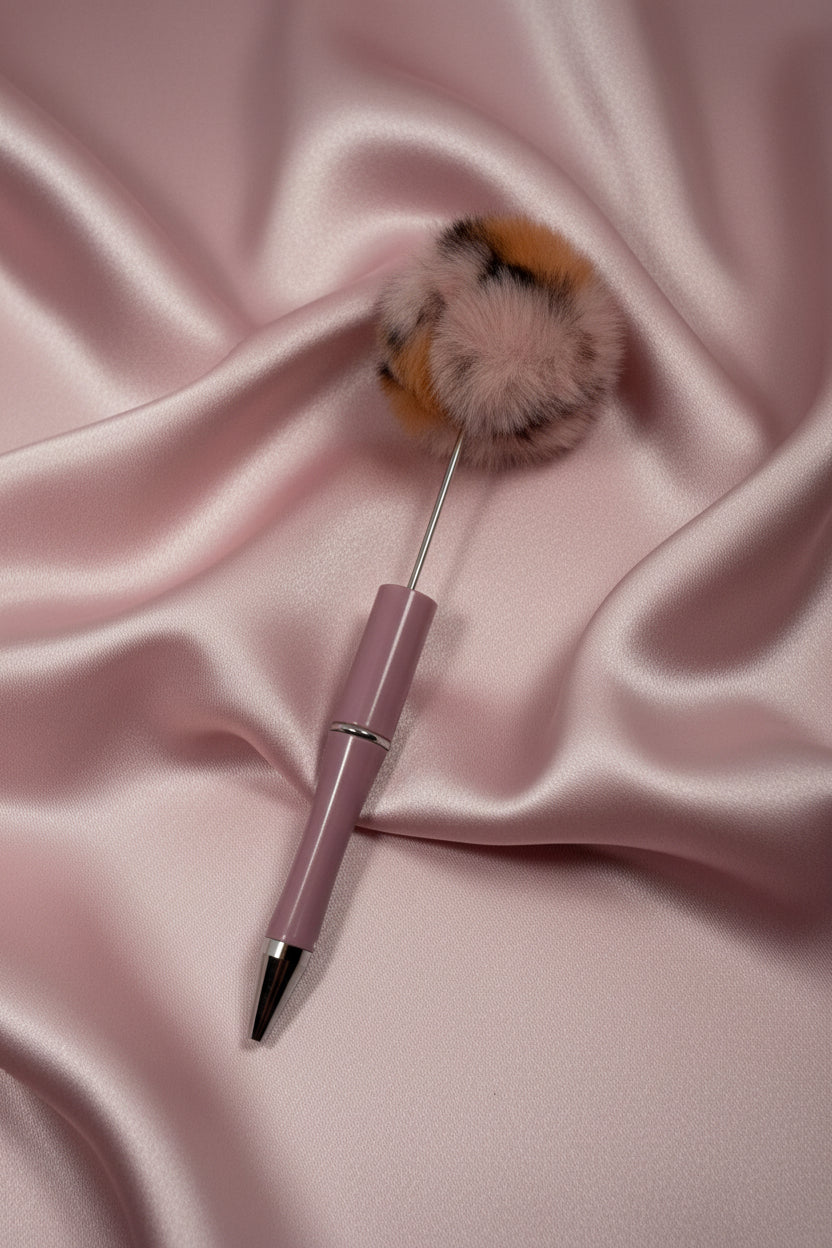 Pink pen with fluffy pom-pom topper on satin fabric, cute stationery accessory
