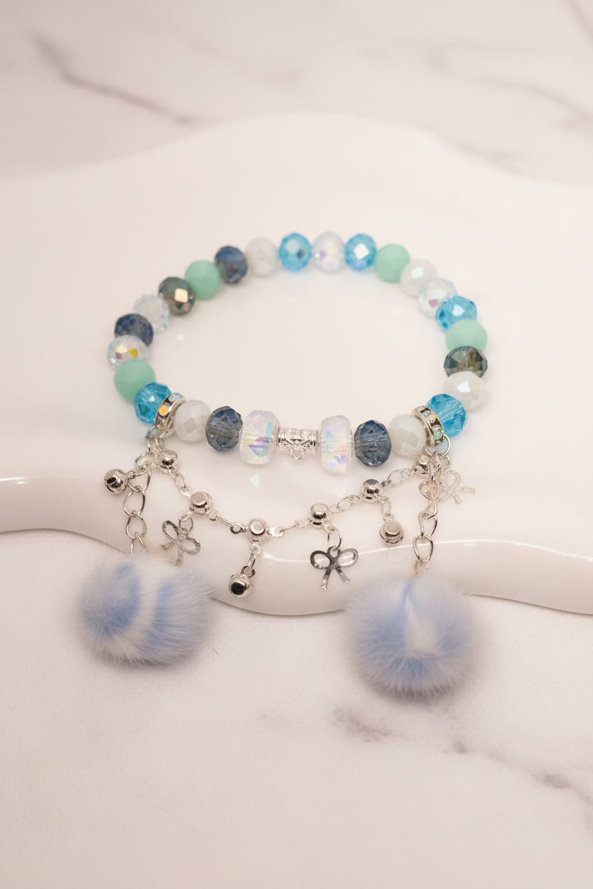 Handmade beaded bracelet with blue, mint, and iridescent beads, silver charms, and fluffy pom poms