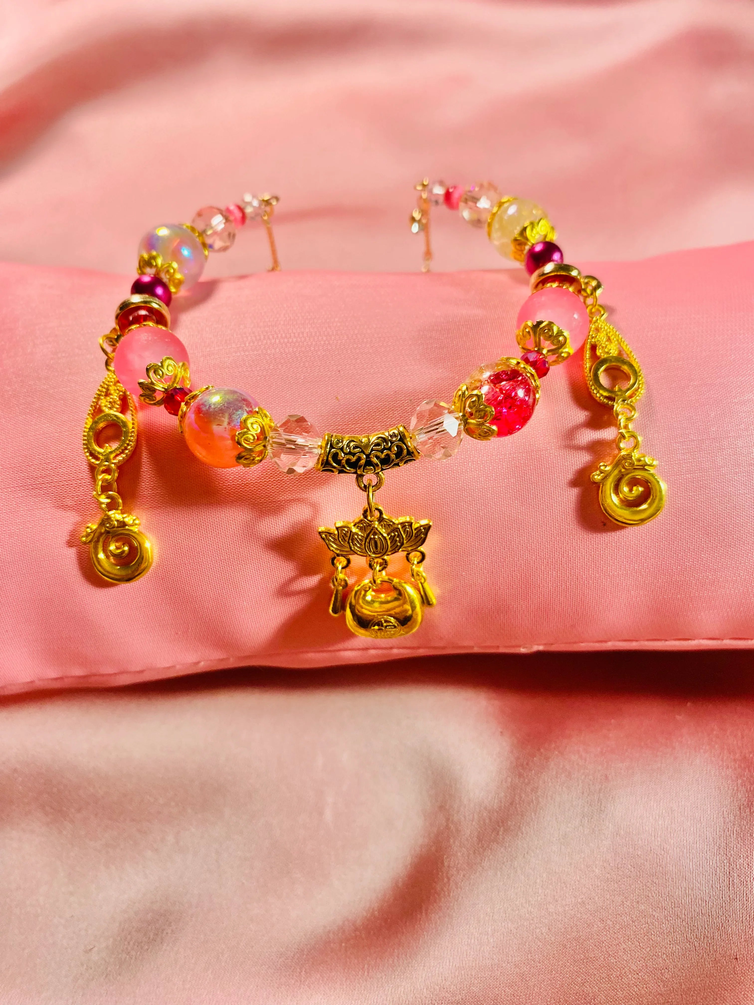 Handmade beaded bracelet with pink, gold, and crystal charms on soft pink fabric