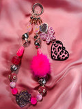 Handmade beaded keychain with pink pom-pom, leopard print hearts, and colorful charms on satin