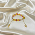 Handmade beaded bracelet with pink and yellow beads, gold leaf charms, on satin fabric