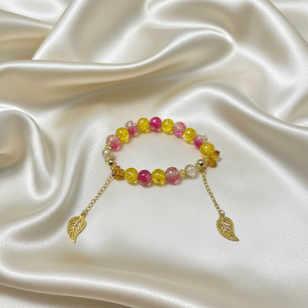Handmade beaded bracelet with pink and yellow beads, gold leaf charms, on satin fabric