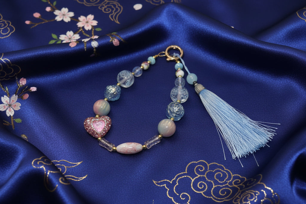 Handmade beaded bracelet with heart charm and blue tassel on embroidered silk, perfect for DIY accessories.