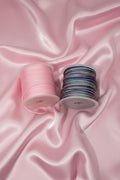 Pink and multicolor beading cord spools on satin fabric for DIY jewelry making