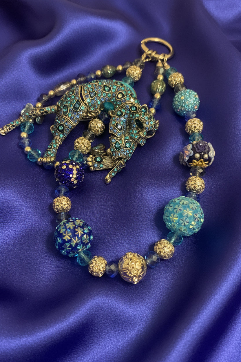 Handmade beaded necklace with ornate elephant pendant, blue and gold beads on purple satin