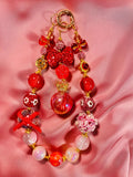 Handmade red beaded keychain with glitter, flowers, crown charm, and gold accents on pink satin