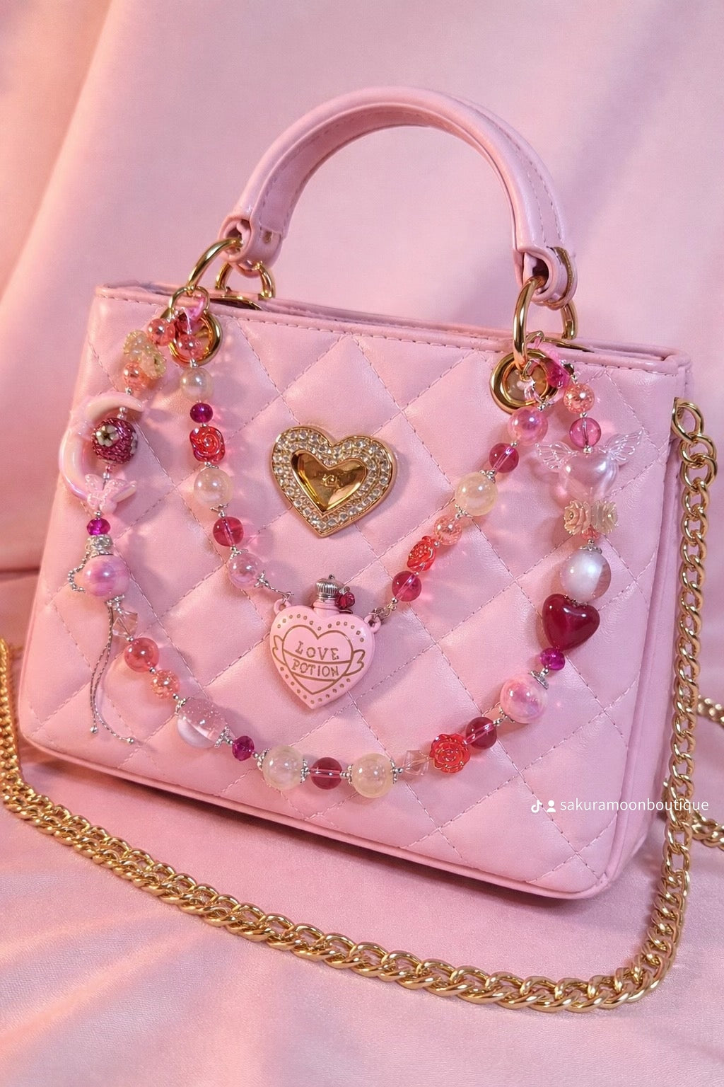 Pink quilted handbag with beaded charm strap, heart locket, and 'Love Potion' pendant, perfect for DIY accessory lovers
