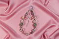 Handmade beaded phone charm with floral beads, crystals, and tassel on pink satin background