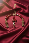 Red beaded necklace with gold chain, bow charm, and tassels on satin fabric