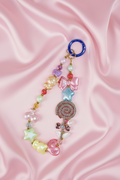 Handmade beaded phone charm with pastel bears, stars, bow, and lollipop on pink satin background