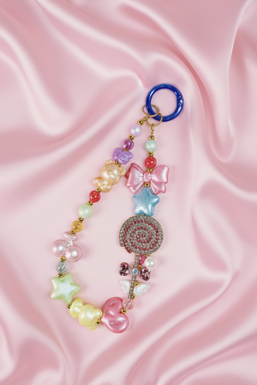 Handmade beaded phone charm with pastel bears, stars, bow, and lollipop on pink satin background