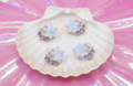 Glitter star earrings with pearls and purple beads, displayed on a seashell against pink iridescent background