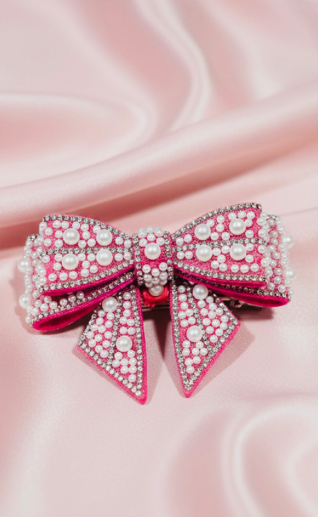 Handmade pink beaded bow hair clip with pearls and rhinestones on satin background