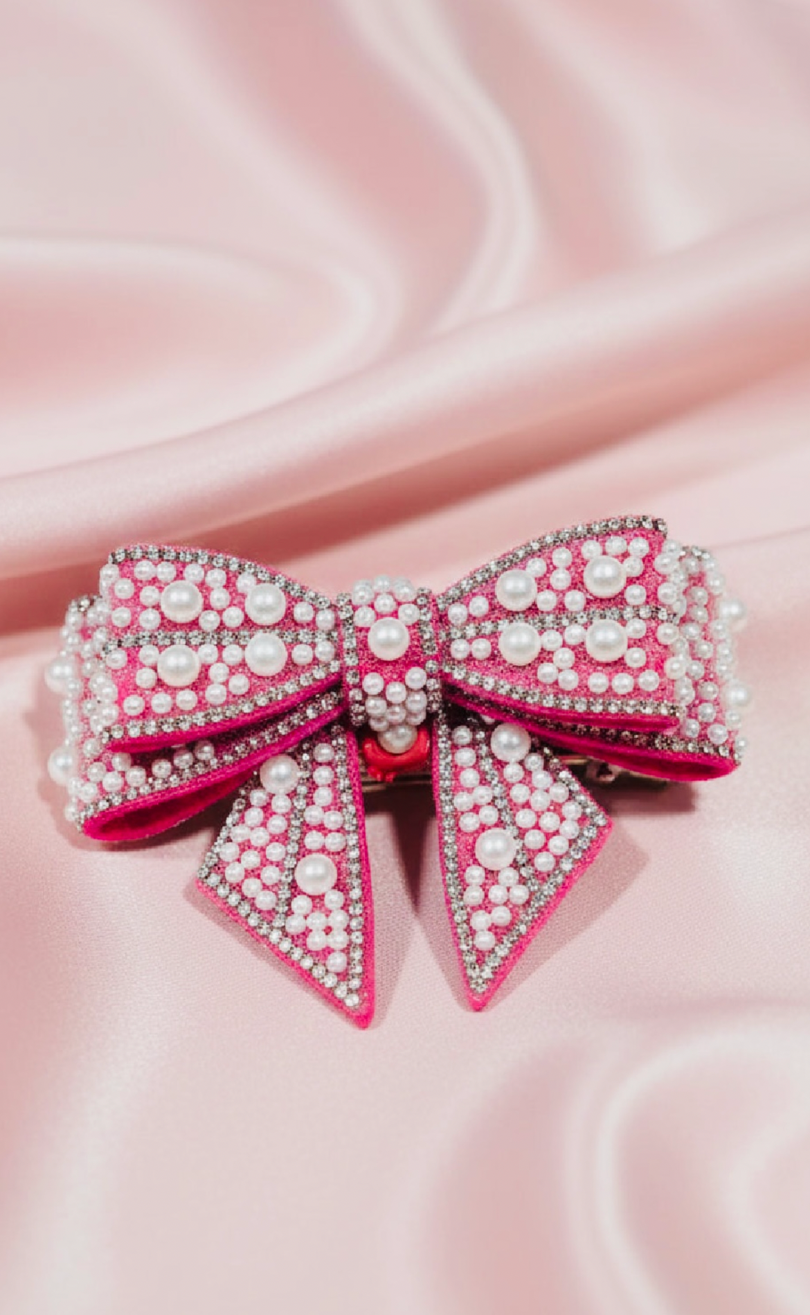 Handmade pink beaded bow hair clip with pearls and rhinestones on satin background